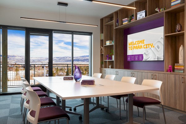 A conference room with a table, chairs, books, and a decorative vase. A screen reads 