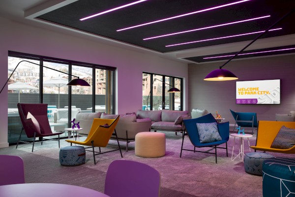 A modern lounge with colorful chairs, sofas, and a large window. Purple lighting and a 