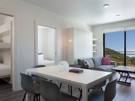 Modern room with a dining table, chairs, sofa, large window with scenic view, bunk beds, open doors, and minimalist decor.