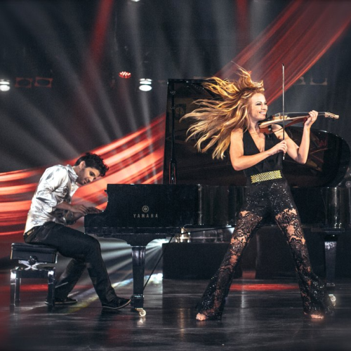 A dynamic performance with a pianist and a violinist on stage, surrounded by dramatic lighting and red drapes, create a vibrant atmosphere.