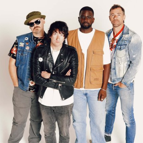 Four individuals in varied casual clothing, including denim and leather, stand against a plain backdrop.