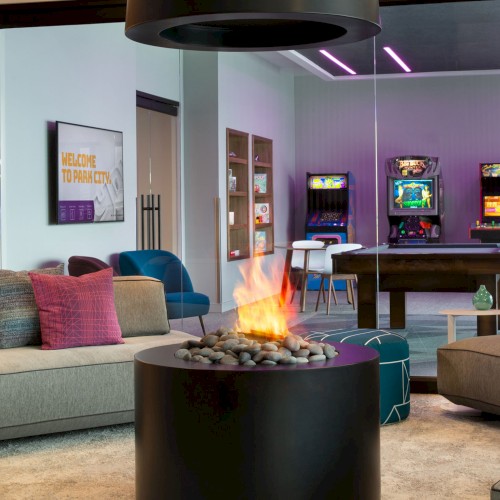 A modern lounge area with sofas, a fireplace, arcade machines, and a pool table, creating a cozy and fun gaming atmosphere.
