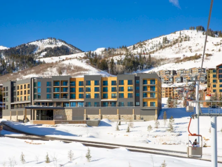 A modern building sits in a snowy mountain landscape, with ski lifts in the foreground and hills in the background.